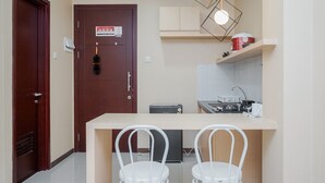 A compact kitchen with a refrigerator, a sink, and a countertop. There are two white chairs in front of the counter. - Gorgeous and Relaxing 1BR Asatti Apartment (Pagedangan)