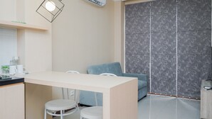 A modern kitchen with a white countertop, two white bar stools, a blue sofa, and a patterned sliding door. - Gorgeous and Relaxing 1BR Asatti Apartment (Pagedangan)