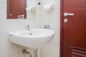 A bathroom with a white sink, a mirror, a wooden door, and a toilet paper holder. - Gorgeous and Relaxing 1BR Asatti Apartment (Pagedangan)