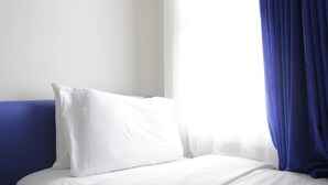 A bed with white bedding and a blue headboard in a room with white walls and a blue curtain. - Fabolous Thematic 2BR Apartment at Parahyangan Residence Near UNPAR (Bandung)