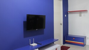 A room with a blue wall, a mounted TV, a white door, and a Superman-themed cabinet. - Fabolous Thematic 2BR Apartment at Parahyangan Residence Near UNPAR (Bandung)