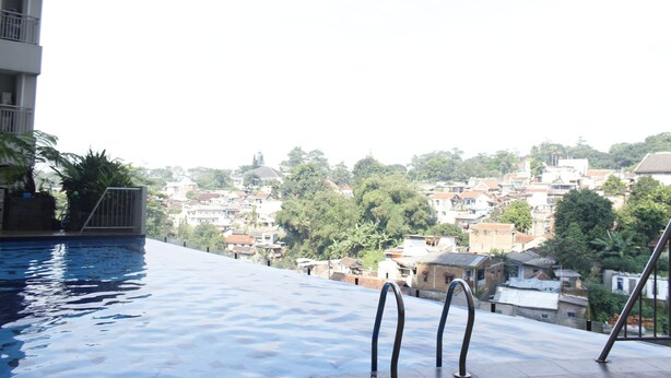 An infinity pool with metal railings, overlooking a densely packed residential area with various buildings and greenery. - Fabolous Thematic 2BR Apartment at Parahyangan Residence Near UNPAR (Bandung)