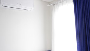 A hotel room with a white wall, a Samsung air conditioner, a blue headboard, and a window with blue curtains. - Fabolous Thematic 2BR Apartment at Parahyangan Residence Near UNPAR (Bandung)