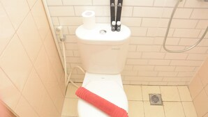 A toilet with a red towel, a toilet paper roll, and two bottles on the tank. - Relaxing Studio at Tifolia Apartment (Jakarta)