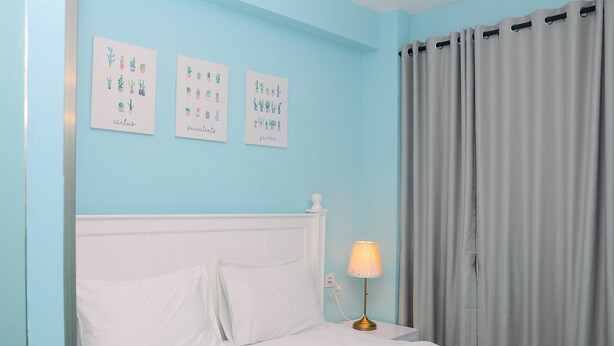 A bedroom with a bed, white bedding, a nightstand with a lamp, and three wall art pieces depicting cacti, succulents, and a garden. - Relaxing Studio at Tifolia Apartment (Jakarta)
