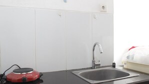 Une cuisine avec un évier, un appareil électroménager rouge et un lit à l’arrière-plan.