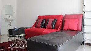 Une chambre d’hôtel moderne avec un canapé rouge et noir, une petite table sur laquelle se trouve un plateau noir, et un tapis rouge.