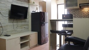 A compact kitchen with a flat-screen TV, a refrigerator, and a bar stool. - Private & Stylish 2BR at Gateway Apartment Ahmad Yani Cicadas (Bandung)
