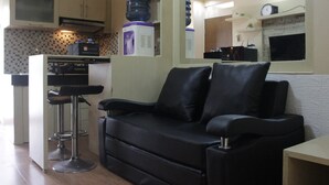 A modern living room with a black leather sofa, a bar stool, and a kitchen area with a microwave, kettle, and water dispenser. - Private & Stylish 2BR at Gateway Apartment Ahmad Yani Cicadas (Bandung)
