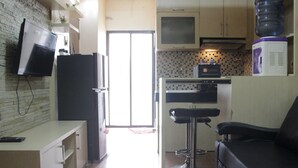 A compact kitchen with a refrigerator, microwave, and water dispenser. A black chair is positioned near the counter. - Private & Stylish 2BR at Gateway Apartment Ahmad Yani Cicadas (Bandung)