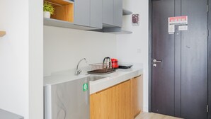 Eine moderne Küche mit weißer Arbeitsplatte, einem Spülbecken und einem roten Wasserkocher. Eine dunkelholztür mit Schloss und eine kleine Pflanze befinden sich auf dem Regal über der Arbeitsfläche.