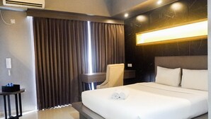 Ein Hotelzimmer mit einem großen Bett, einem Schreibtisch mit Stuhl, einem Schminktisch und einem Fenster mit Vorhängen.