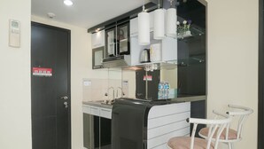 Cocina compacta con estufa integrada, microondas y cafetera. Hay dos taburetes blancos con asientos acolchados.