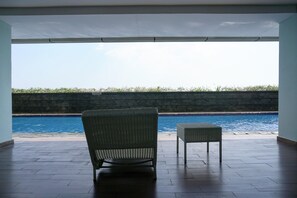 A covered outdoor area with a pool, a wicker chair, and a small table. - Homey 2BR Apartment @ Belmont Residence (Jakarta)