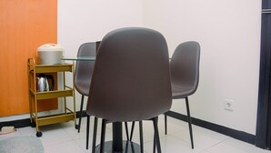 Een kamer met een tafel en stoelen, een klein plankje met een waterkoker en een voorraadpot, en een deur met een lichtschakelaar.