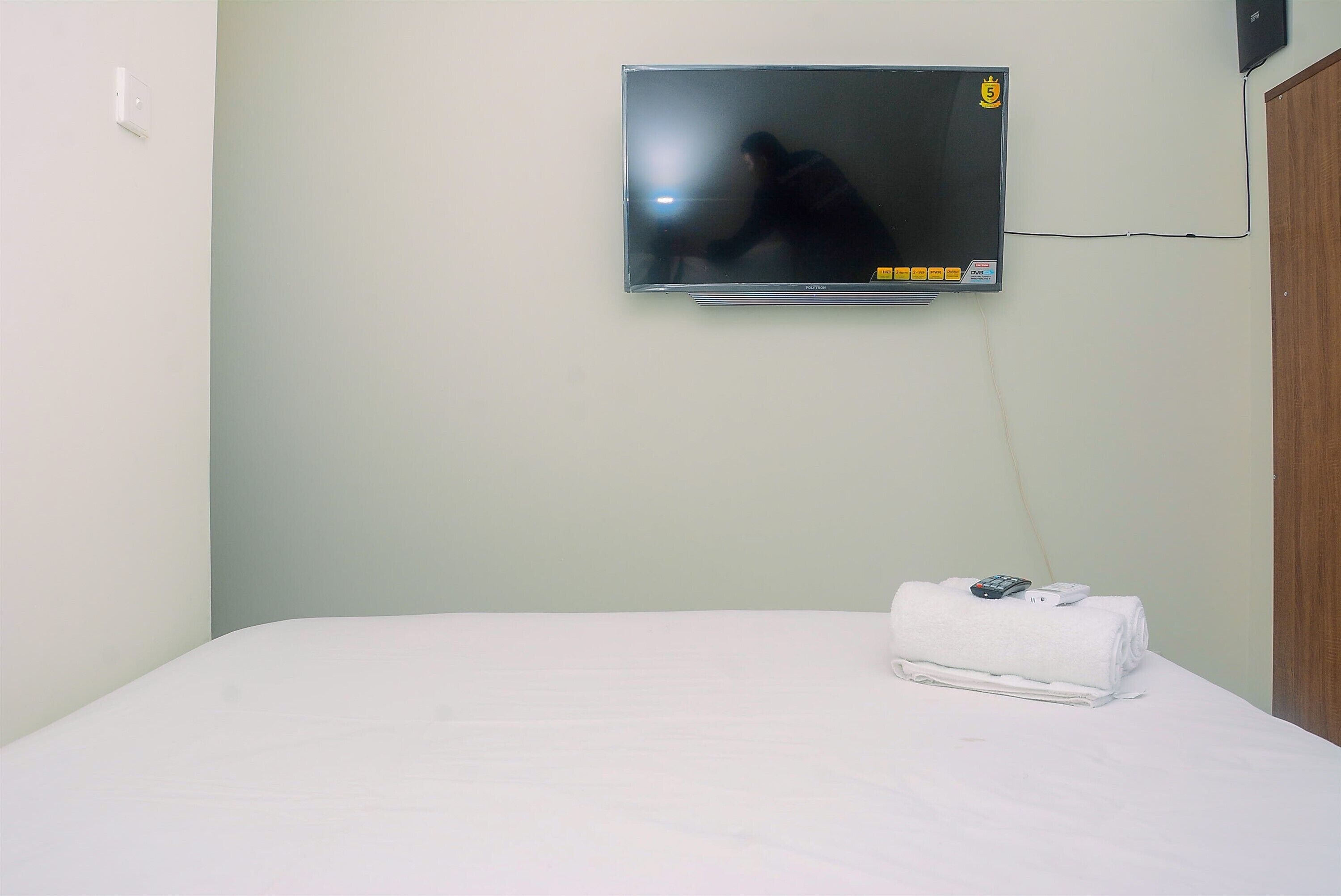 A hotel room with a bed, a television mounted on the wall, and a towel on the bed.