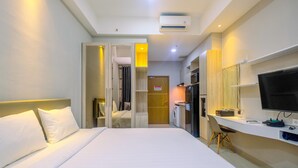 A hotel room with a bed, a desk, a TV, and a washing machine. - Homey and Warm Studio Apartment Oasis Cikarang (Cikarang)