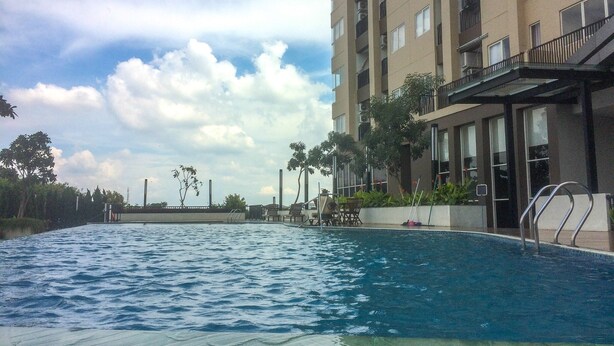 A swimming pool adjacent to a multi-story building with balconies. - Homey and Warm Studio Apartment Oasis Cikarang (Cikarang)