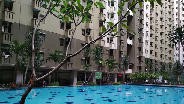 A swimming pool with blue tiles and palm trees in the foreground, surrounded by a high-rise building with balconies. - Minimalist 2BR Apartment at Gateway Ahmad Yani Cicadas (Bandung)