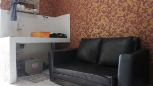 A small living area with a black leather sofa, a white sink with a dish rack above, and patterned wallpaper. - Minimalist 2BR Apartment at Gateway Ahmad Yani Cicadas (Bandung)