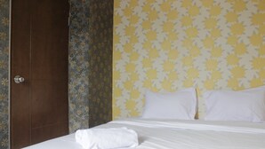 A hotel room with a bed, white linens, a wooden door, and floral wallpaper. - Minimalist 2BR Apartment at Gateway Ahmad Yani Cicadas (Bandung)