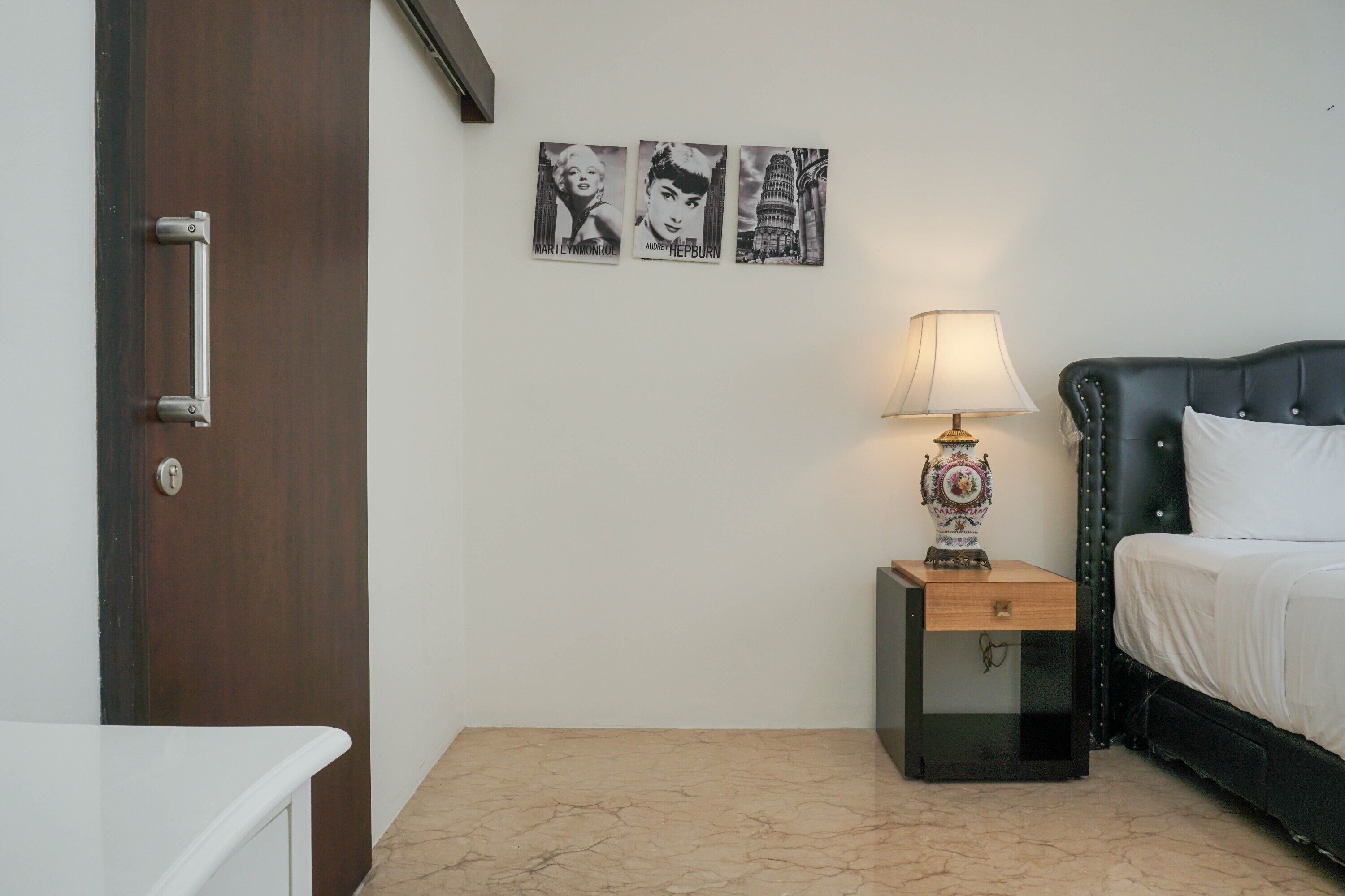 A bedroom with a bed, a nightstand with a lamp, and three framed pictures on the wall.