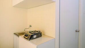 A small kitchenette with a sink, a stove, and cabinets. - New Room Studio at Green Pramuka Apartment (Jakarta)