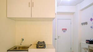 A compact kitchen with a sink, a toaster, and a door with a fire safety sign. - New Room Studio at Green Pramuka Apartment (Jakarta)