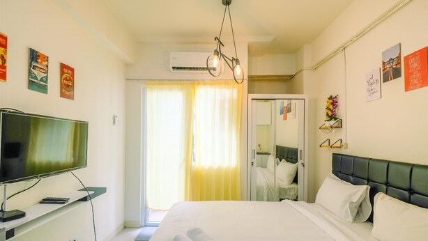 A hotel room with a bed, a TV, a mirror, and a door leading to a balcony. - New Room Studio at Green Pramuka Apartment (Jakarta)