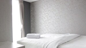 Ein ordentlich bezogenes Bett mit weißer Decke und einem gefalteten weißen Handtuch, ein Nachttisch aus Holz und eine Wand mit Muster.
