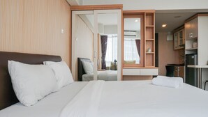 A hotel room with a large bed, a wooden wardrobe, a small desk, and a kitchenette. - Elegant and Relaxing Studio Apartment H Residence (Jakarta)