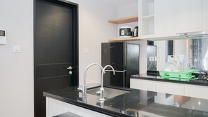 A modern kitchen with a black countertop, stainless steel sink, and a black door. - Marvelous 1BR at The Branz Apartment (Pagedangan)