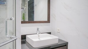 A bathroom with a white sink, dark countertop, and a mirror with a wooden frame. - Marvelous 1BR at The Branz Apartment (Pagedangan)