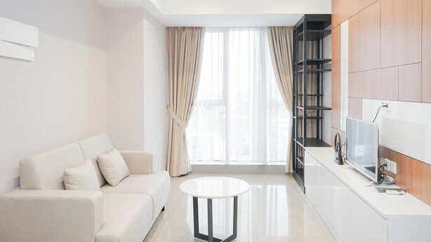 A modern living room with a white sofa, a round coffee table, and a TV on a wooden cabinet. - Marvelous 1BR at The Branz Apartment (Pagedangan)