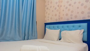 A neatly made bed with a blue headboard, white pillows, and a white towel. - Spacious and Comfy 2BR Bassura City Apartment (Jakarta)