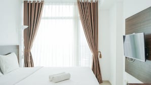 A hotel room with a bed, curtains, a TV, and a wooden headboard. - Modern Studio Apartment at Tree Park Cikokol (Tangerang)