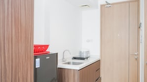 A compact kitchen with a refrigerator, sink, and wooden cabinets. - Modern Studio Apartment at Tree Park Cikokol (Tangerang)