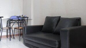 A black leather sofa, a glass table with chairs, and a blue storage basket in a room with white walls and tiled flooring. - Pleasant 2BR Apartment at Gateway Ahmad Yani (Bandung)