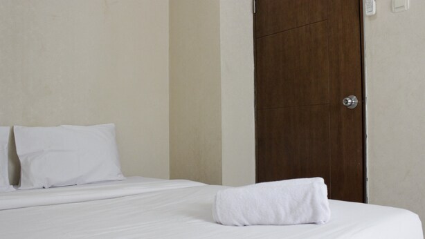 A neatly made bed with white linens and a folded towel, a wooden door, and a plain wall. - Pleasant 2BR Apartment at Gateway Ahmad Yani (Bandung)