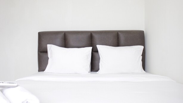 Una cama con cabecera tapizada en gris y dos almohadas blancas.