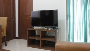 Una sala de estar con un televisor sobre un pedestal de vidrio, un sofá marrón y una puerta de madera.