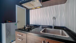 A modern kitchen with a stainless steel sink, a built-in stove, and a vent hood above the stove. - Comfort 1BR with Study Room Green Pramuka Apartment (Jakarta)