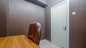 A conference room with a wooden table, a plastic-covered chair, and a closed door. - Comfort 1BR with Study Room Green Pramuka Apartment (Jakarta)
