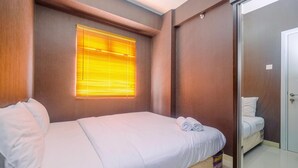 A hotel room with a bed, a window with blinds, a mirror, and a door. - Comfort 1BR with Study Room Green Pramuka Apartment (Jakarta)