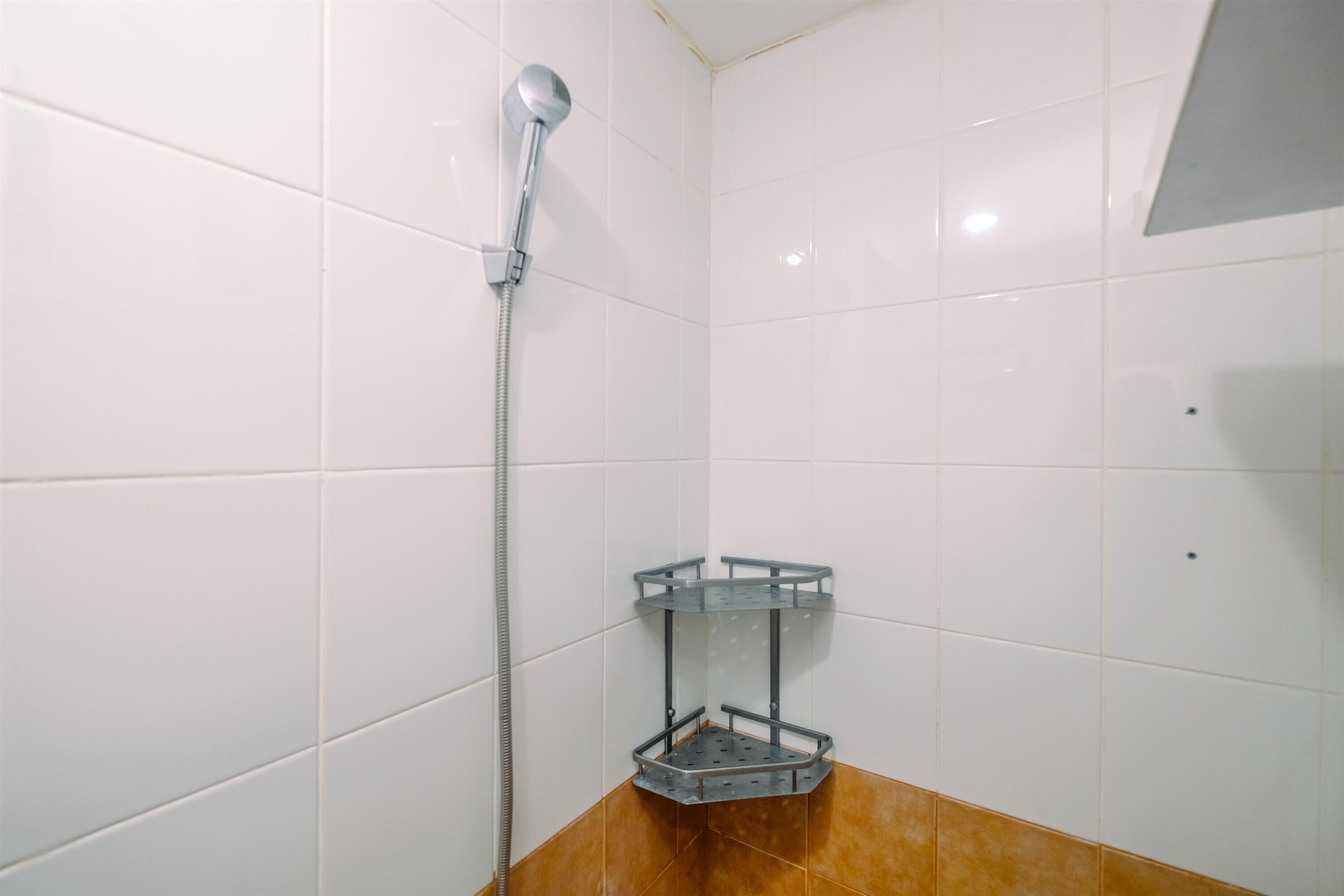A bathroom with white tiles, a shower, and a corner shelf.