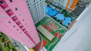 Vista aérea de un edificio alto con fachada rosa, junto a un complejo deportivo con piscina y canchas de tenis.