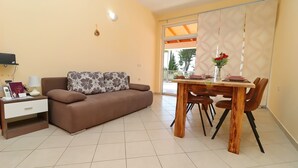 A living room with a brown sofa, a wooden dining table with chairs, and a TV on a stand. - Apartments Villa Michele (Orebic)