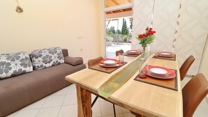 A dining area with a wooden table set for two, a sofa with patterned cushions, and a view of the outdoors through a glass door. - Apartments Villa Michele (Orebic)