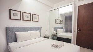 A hotel room with a large bed, a wardrobe, a bedside table with a lamp, and framed pictures on the wall. - Premium 2BR Apartment near Marvell City Mall at The Linden (Surabaya)
