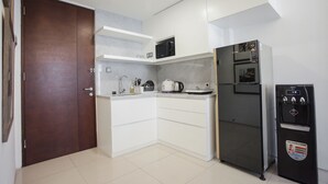A compact kitchen with white cabinets, a microwave, a refrigerator, and a water dispenser. - Premium 2BR Apartment near Marvell City Mall at The Linden (Surabaya)
